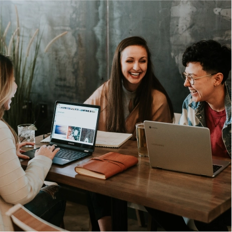 Varias personas sonrientes mientras trabajan en una mesa con ordenadores y cuadernos